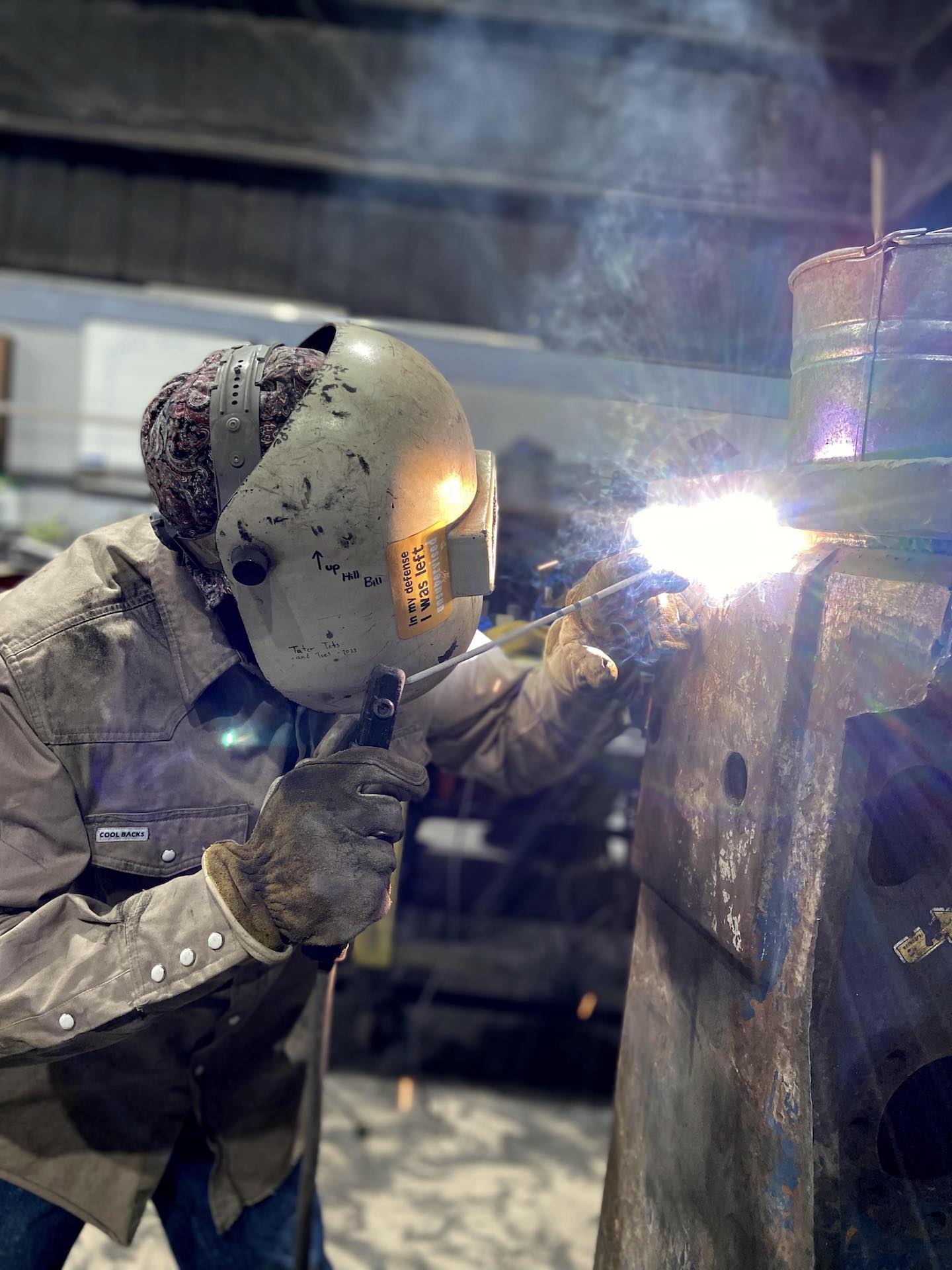 A man in a welding mask sewing up some seams with fire.